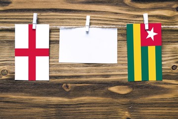 Hanging flags of England and Togo attached to rope with clothes pins with copy space on white note paper on wooden background.Diplomatic relations between countries.