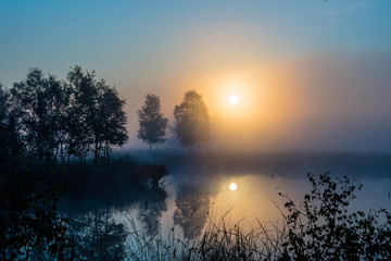 Obraz na płótnie Canvas Sunrise in the misty Pietzmoor with a gently lying lake, some trees and the reflection in the moor lake