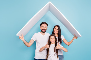 Portrait of beautiful three people school girl with brown hair hold paper card roof move to new house approve feedback show thumb-up wear white t-shirt isolated over blue color background