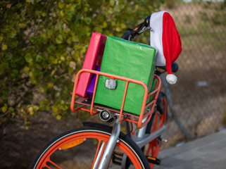 Orange bicycle with basket on the front, loaded with gifts and a Santa Claus cap attached to the...