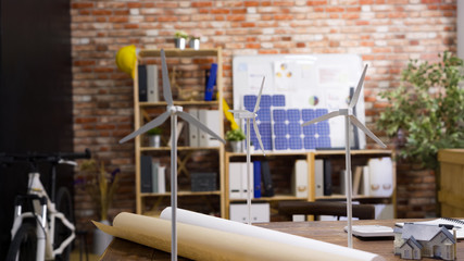 Construction office engineer empty working table. modern eco friendly workplace in architect company indoors with red brick wall. windmill and 3D house miniature on desk for green energy building. © PRPicturesProduction