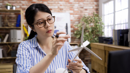 Portrait of asian beautiful woman architect working on ecological construction project in her office. girl employee holding and looking models of wind turbines. confident female engineer think ideas.