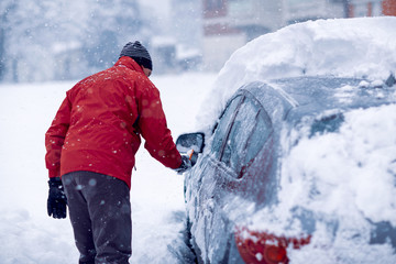 Snow covered car. man brushing the snow off his car on a winter day