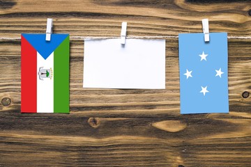 Hanging flags of Equatorial Guinea and Micronesia attached to rope with clothes pins with copy space on white note paper on wooden background.Diplomatic relations between countries.