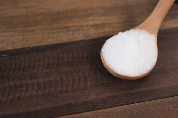 heap of white sugar in a wooden ladle over wooden table. concept of unhealthy eating and diabetes