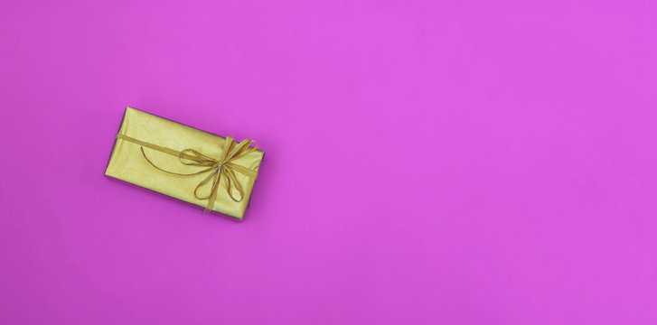 Golden box with a bow. Gift on a colored pink background. Great design for any purposes. Fashion, glamor background. New year, Christmas design