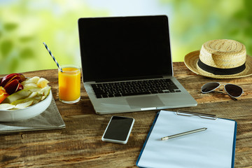 Blank screens of laptop and smartphone on a wooden table outdoors with nature on background, mock up. Fruits and fresh juice near by. Concept of creative workplace, business, freelance. Copyspace.