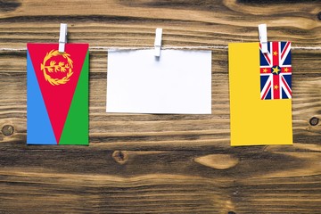 Hanging flags of Eritrea and Niue attached to rope with clothes pins with copy space on white note paper on wooden background.Diplomatic relations between countries.
