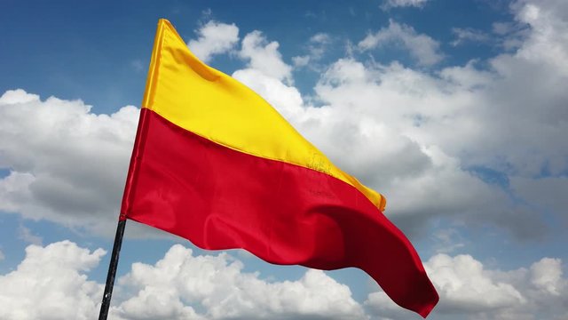Close up of the official flag of the South Indian state of Karnataka flying against the sky and clouds in the background