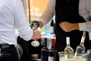 a waiter filling a glass with wine over the counter for a customer