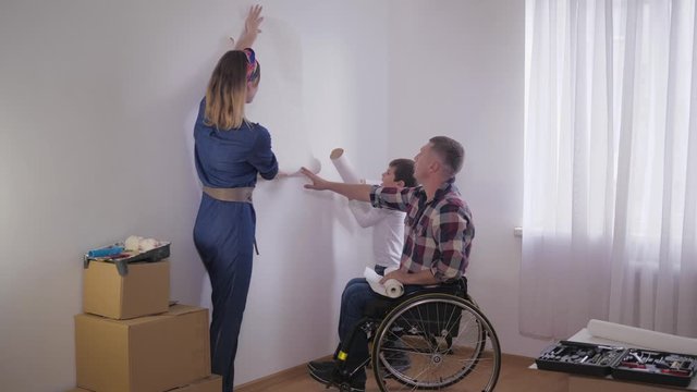 happy family with handicapped father in wheelchair amicably choose new wallpaper in room during repair