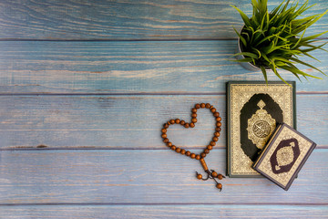 Flat lay view of vase, tasbih or rosary beads and Holy book of Al Quran with arabic calligraphy meaning of Al Quran over wooden background. Selective focus and crop fragment
