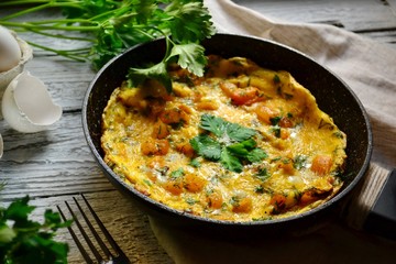 Appetizing omelet on a wooden light background. Omelet with yellow tomato, sweet yellow pepper and parsley leaves in a pan. Tasty breakfast.