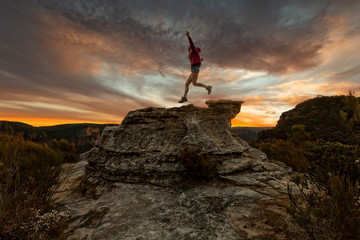 Active woman jumping on mountain cliffs at sunset