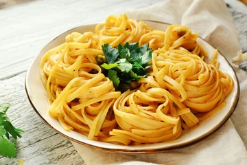 Pasta in a beautiful white plate. Pasta on a light wooden background. Spaghetti with parsley leaves. Macaroni, parsley, lemon, sweet yellow pepper.