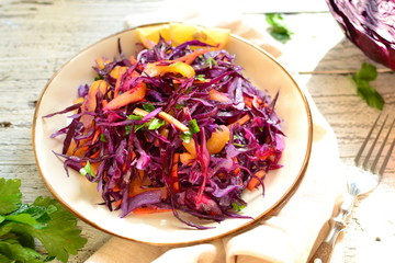 Fresh spring salad with red cabbage, sweet pepper and carrots and parsley. Salad with cabbage in a beautiful plate. Wood background. Sunlight. Top view. Delicious healthy food made from vegetables.