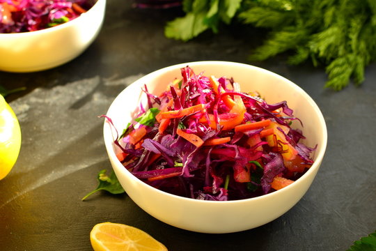 Fresh spring salad with red cabbage, sweet pepper, carrots and parsley leaves. Salad with cabbage in a white bowl. Dark black concrete background on the table. Sunlight. Top view. healthy food
