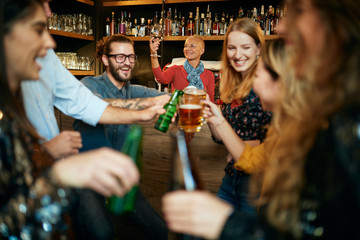 Friends standing in bar and toasting with beer.