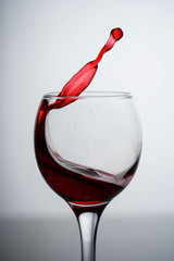 splashes of red wine in a glass on a black glossy glass on a white background