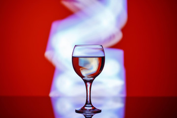 a glass with a drink on a beautiful red background illuminated with colored light.