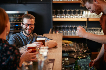 Friends standing next to bar counter in pub and drinking beer. Night out.