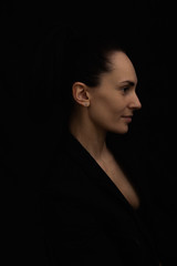 Profile of a beautiful brunette in a black jacket on a black background