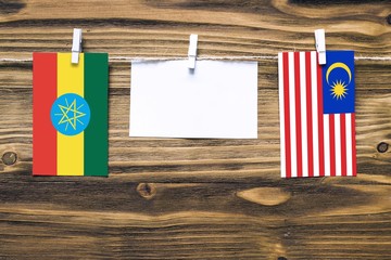 Hanging flags of Ethiopia and Malaysia attached to rope with clothes pins with copy space on white note paper on wooden background.Diplomatic relations between countries.