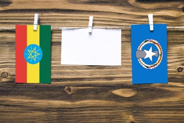 Hanging flags of Ethiopia and Northern Mariana Islands attached to rope with clothes pins with copy space on white note paper on wooden background.Diplomatic relations between countries.