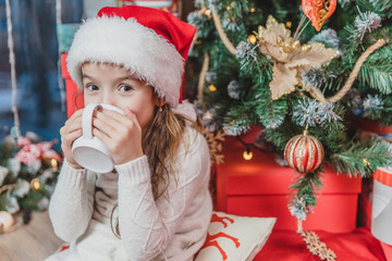 Close-up photo of cute smiling girl sitting cozy at home, drinking hot chocolate at christmas tree...