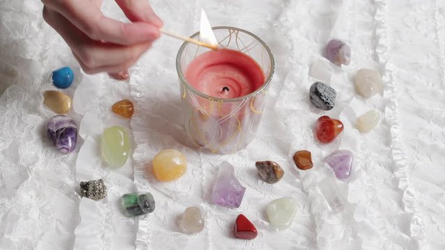 A hand lights a red candle on an altar with crystals and white lace