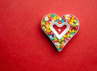 Creative layout of heart shape with colorful candies over red background and place for text