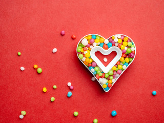 Creative layout of heart shape with colorful candies over red background