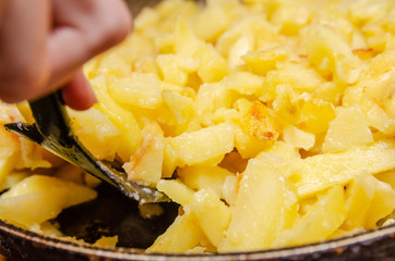 woman's hand with a black spatula stirs potatoes while frying in a frying pan close up