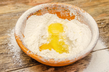 brown bowl of flour and egg stands close up on a wooden background, top view