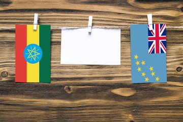 Hanging flags of Ethiopia and Tuvalu attached to rope with clothes pins with copy space on white note paper on wooden background.Diplomatic relations between countries.