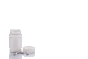 A vial of pills stands on a mirror surface on a white background on the left with a place for text.