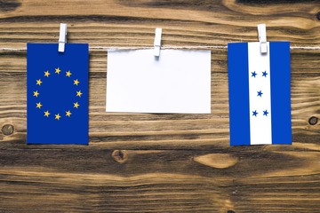 Hanging flags of European Union and Honduras attached to rope with clothes pins with copy space on white note paper on wooden background.Diplomatic relations between countries.