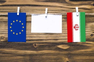 Hanging flags of European Union and Iran attached to rope with clothes pins with copy space on white note paper on wooden background.Diplomatic relations between countries.