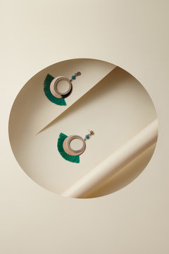 Subject shot of crystal earrings with a turquois bead with a dangling golden embossed ring with a green fringe. The earrings are isolated on the ivory white surface with geometric design. 