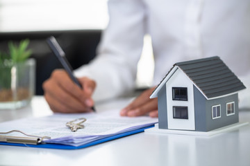 Businessmen and customers are signing home purchase agreements. Hand holding the pen signing purchase contract. Gray roof houses and keys placed close to each other.Real estate mortgage home purchase.