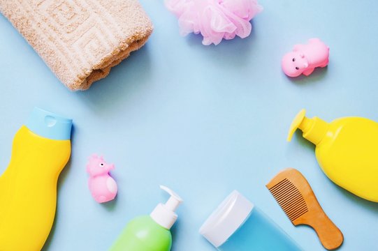 Flat lay photo baby shampoo, shower gel, liquid soap, wooden comb, sponge, towel and rubber toys on a light blue background