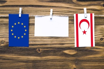 Hanging flags of European Union and Northern Cyprus attached to rope with clothes pins with copy space on white note paper on wooden background.Diplomatic relations between countries.