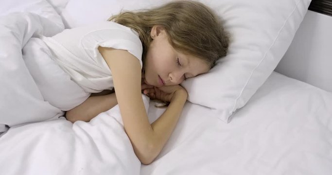 Girl child ten years old with long curly blond hair sleeping in white bed on pillow