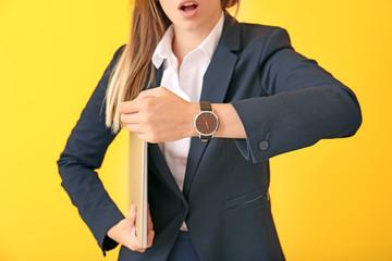 Young businesswoman with laptop and watch on color background
