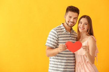 Fototapeta na wymiar Portrait of happy young couple with paper heart on color background