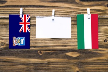 Hanging flags of Falkland Islands and Hungary attached to rope with clothes pins with copy space on white note paper on wooden background.Diplomatic relations between countries.