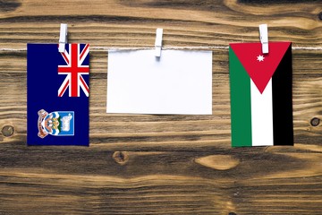 Hanging flags of Falkland Islands and Jordan attached to rope with clothes pins with copy space on...