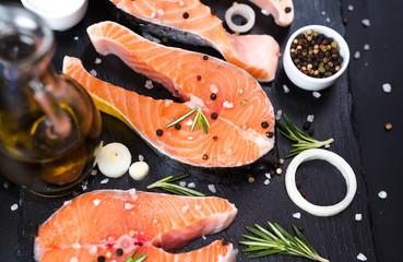 raw salmon steak on a dark stone background with onions, rosemary, spices, concept diet,...
