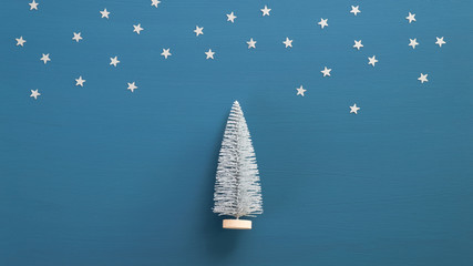 Christmas tree and silver confetti stars on blue background. Minimal winter holidays concept. Flat lay composition, top view.