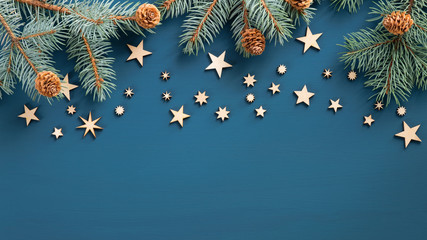 Christmas frame. Top view fir tree branches with cones and wooden handmade stars over blue background. Xmas or New Year banner mockup, greeting card template.